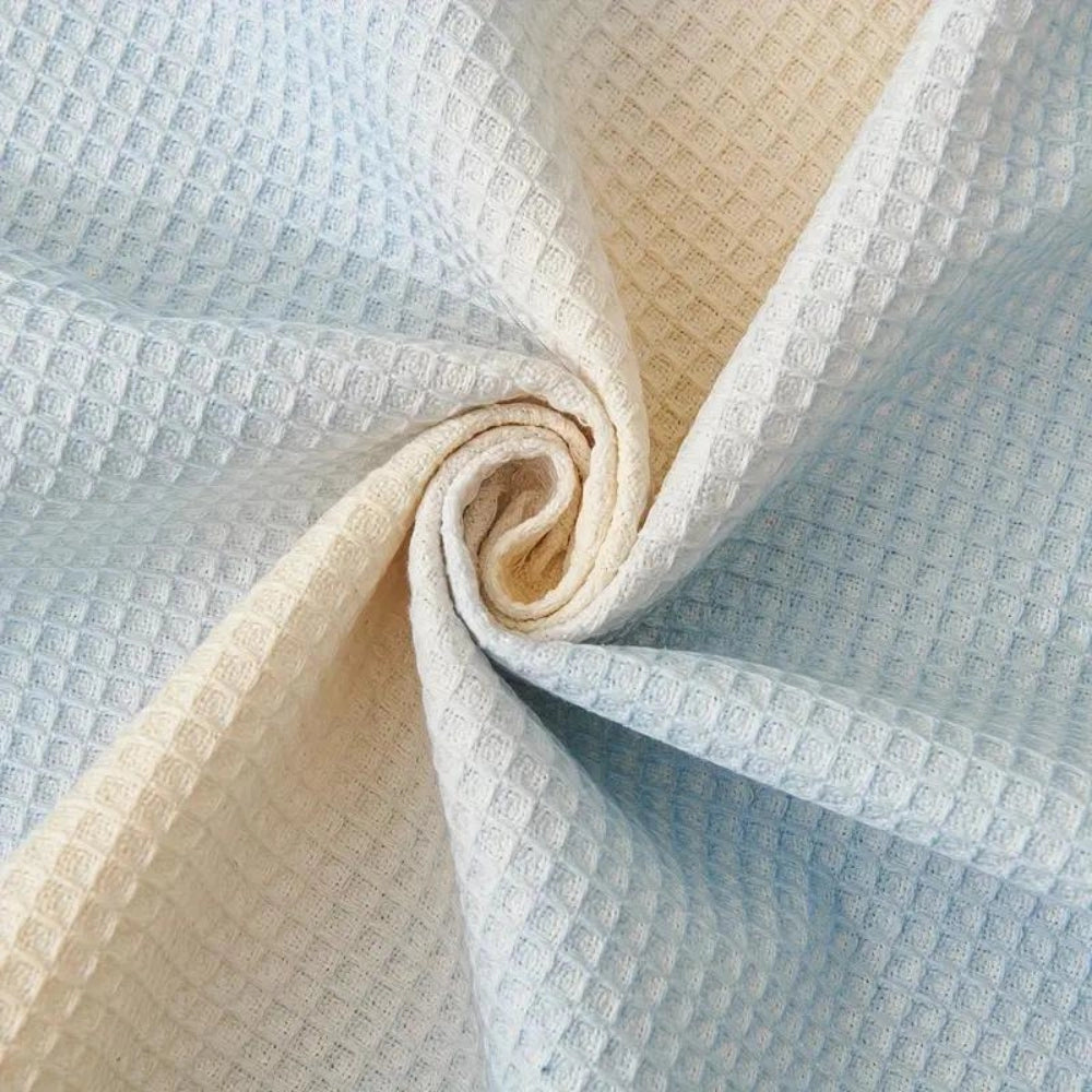 Lightweight pastel blue bedspread made from textured cotton with a fringed edge, displayed on a bed.