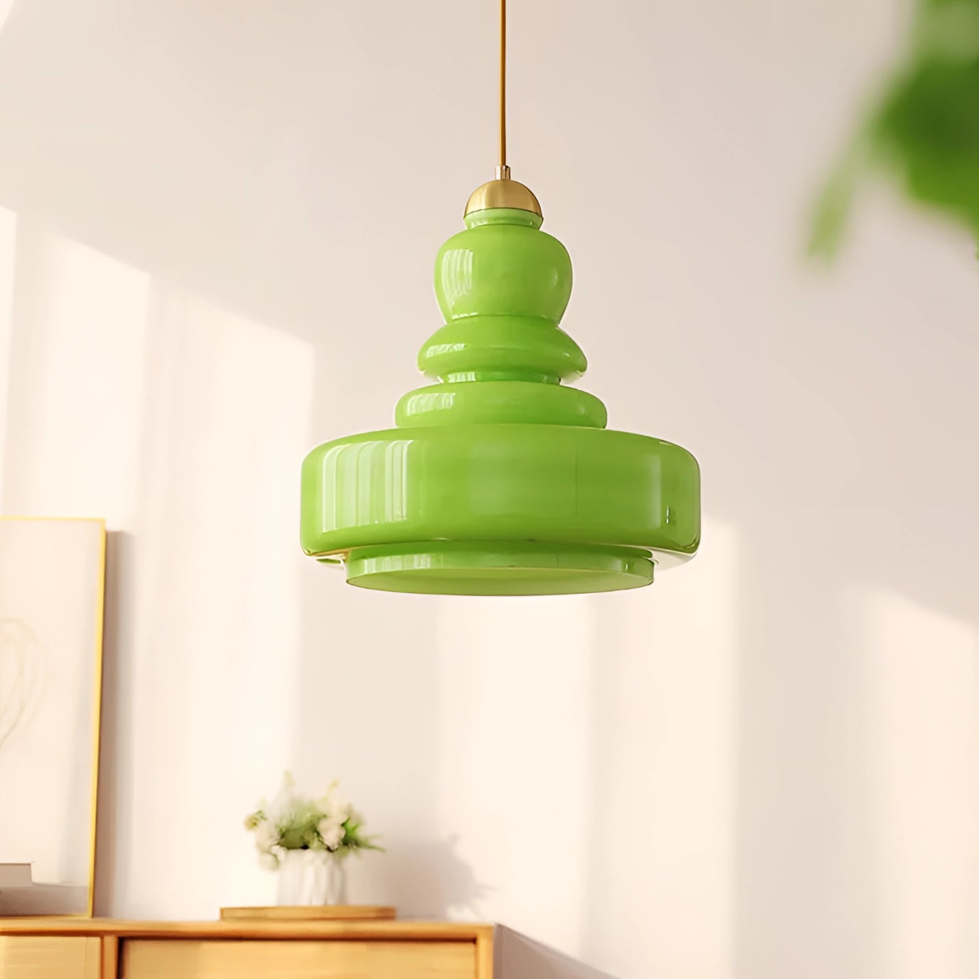 Lime green modern pendant light made of glass and iron, hanging from ceiling, illuminating a Scandinavian-styled kitchen. Houseplants and wooden shelves in the background.