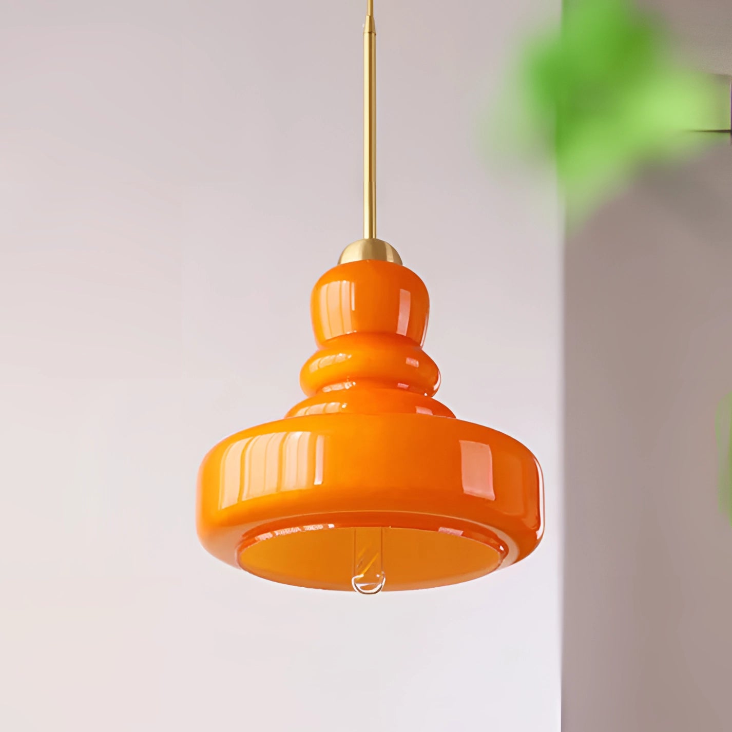 Modern orange glass and brass pendant light with a tiered Scandinavian design, hanging from the ceiling in a kitchen setting.