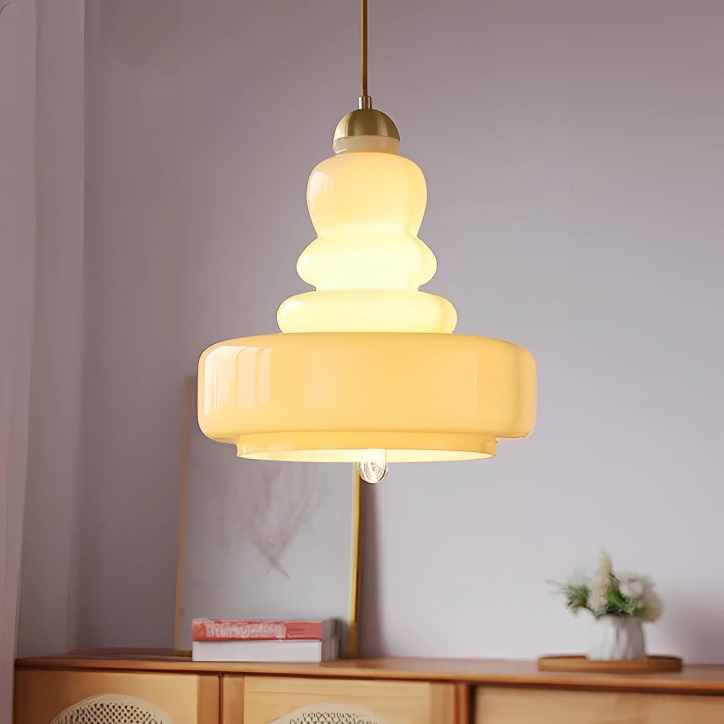 Lime green modern pendant light with tiered Scandinavian design, featuring a beige yellow glass and brass finish, hanging above a wooden table with houseplants and flowerpots in the background.