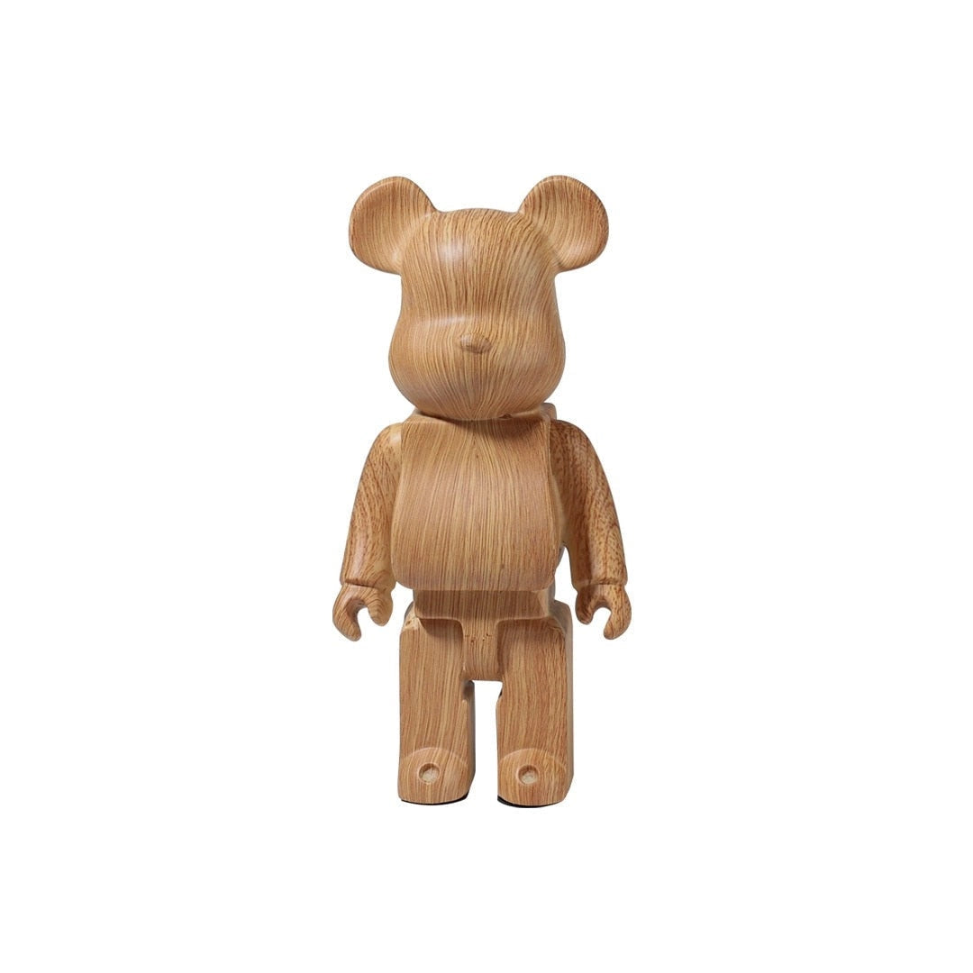 
A limited edition Bearbrick designer art toy figurine made of clear vinyl with a wood sample variant, showcasing a brown color reminiscent of wood, featuring an animal-like design with a snout and resembling a fawn, positioned in a standing gesture similar to a terrestrial animal or working animal figure.