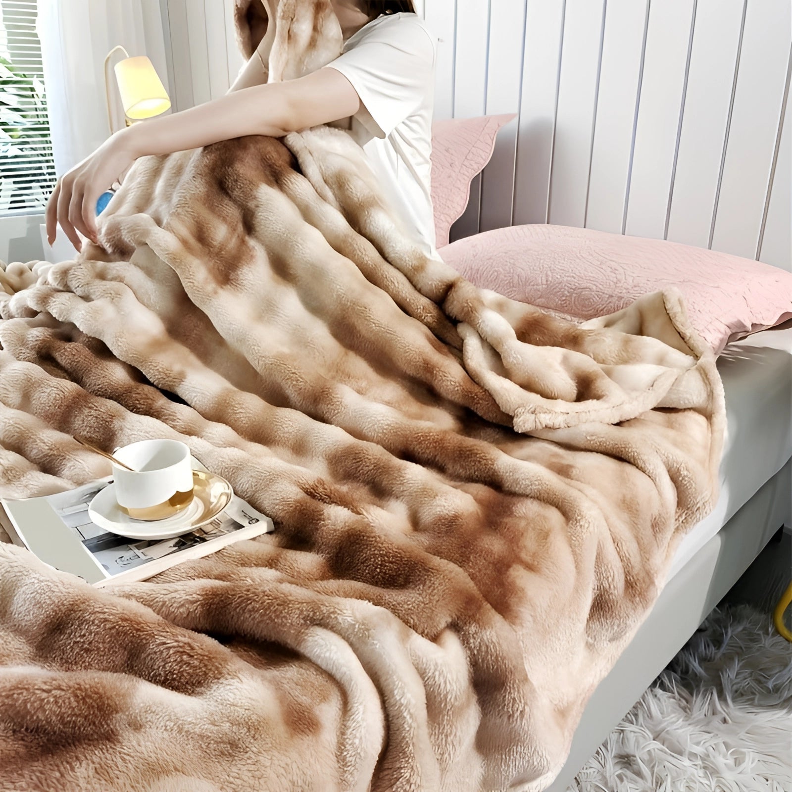 Luxurious faux fur blanket in a soft plush texture draped over a cozy bed, featuring a rich brown color and measuring 200 x 230 cm. The blanket is styled with a subtle pattern and rests on a hardwood surface, contributing to a warm and inviting decor. A hand with a sleeve is gently touching the blanket, emphasizing its comfort and softness.