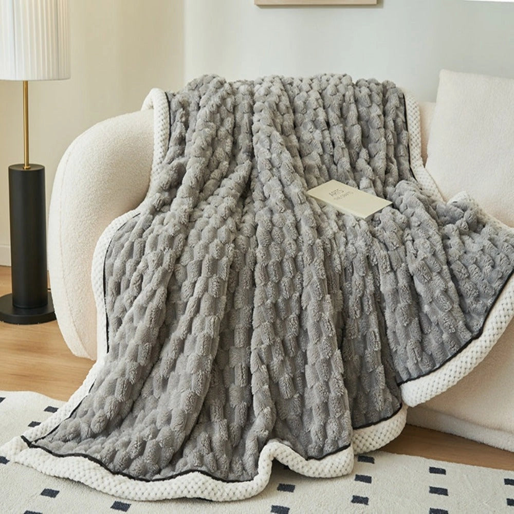 Luxurious pink blush throw blanket with a zigzag pattern, made from soft plush fleece, draped over a wooden chair in a stylish interior space with grey flooring.