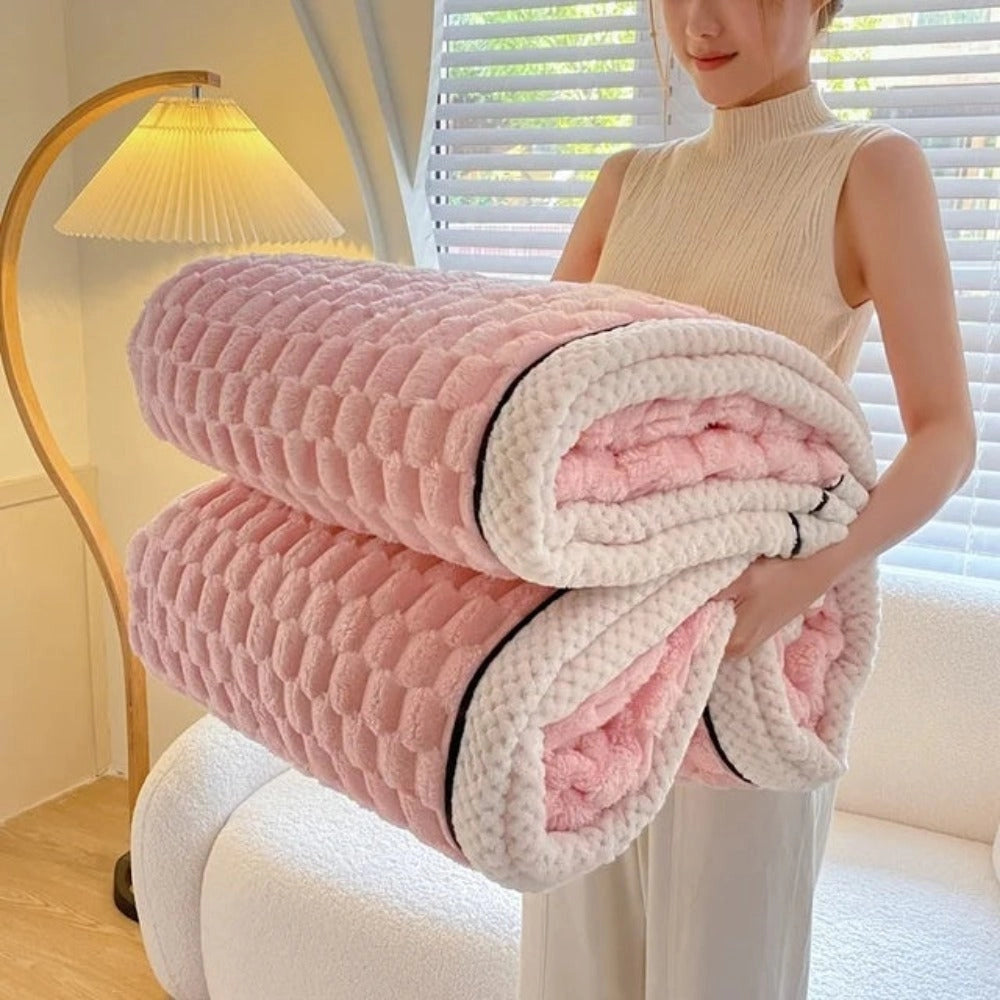 Luxurious pink blush throw blanket made of soft plush fleece with a zigzag pattern, draped over a person's legs and hand, illustrating comfort and warmth.