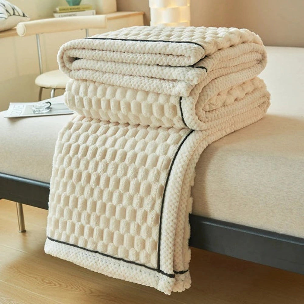 Luxurious Ivory Cream throw blanket with a soft plush fleece and zigzag pattern, draped over a beige rectangular chair on hardwood flooring next to a wicker basket.