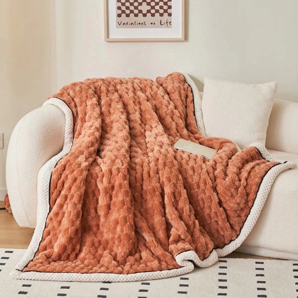 Luxurious pink blush throw blanket with a soft plush fleece texture and zigzag pattern draped over an orange couch in a stylish interior setting.