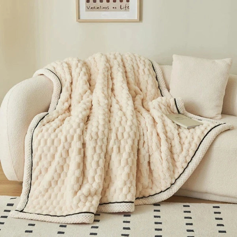 Luxurious pink blush throw blanket with a soft plush fleece texture, featuring a zigzag pattern, laid out on a wooden table with grey and beige elements in the background.