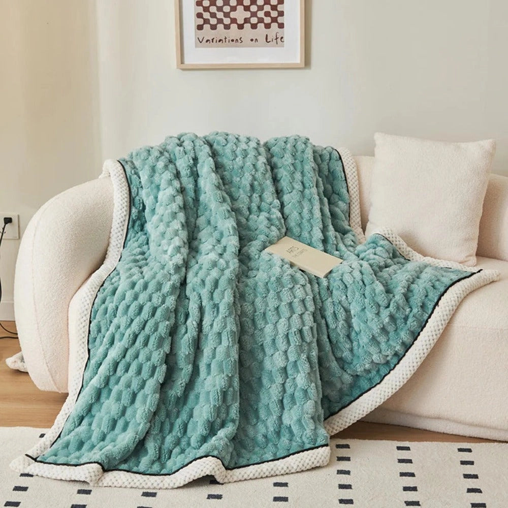 Luxurious pink blush throw blanket with a soft plush fleece texture and zigzag pattern draped over the back of a grey couch.