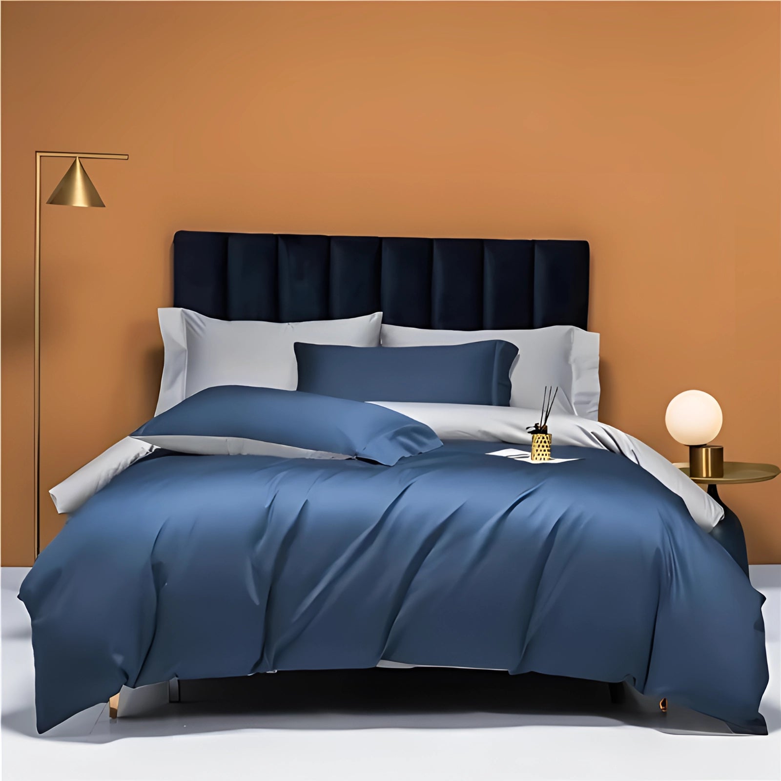 Luxury king-sized bedding set in marine blue Egyptian cotton featuring pillows on a bed with a wooden frame, accompanied by a bedside lamp on a grey floor.