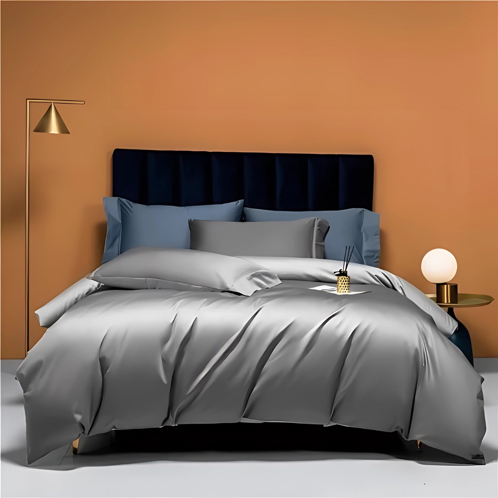 Luxury bedding set in silver, featuring high-end Egyptian cotton linens on a king-sized bed with a sleek grey wooden bed frame. The room includes a lamp beside the bed and is decorated with a comfortable arrangement of pillows on a rectangular mattress over a smooth flooring.