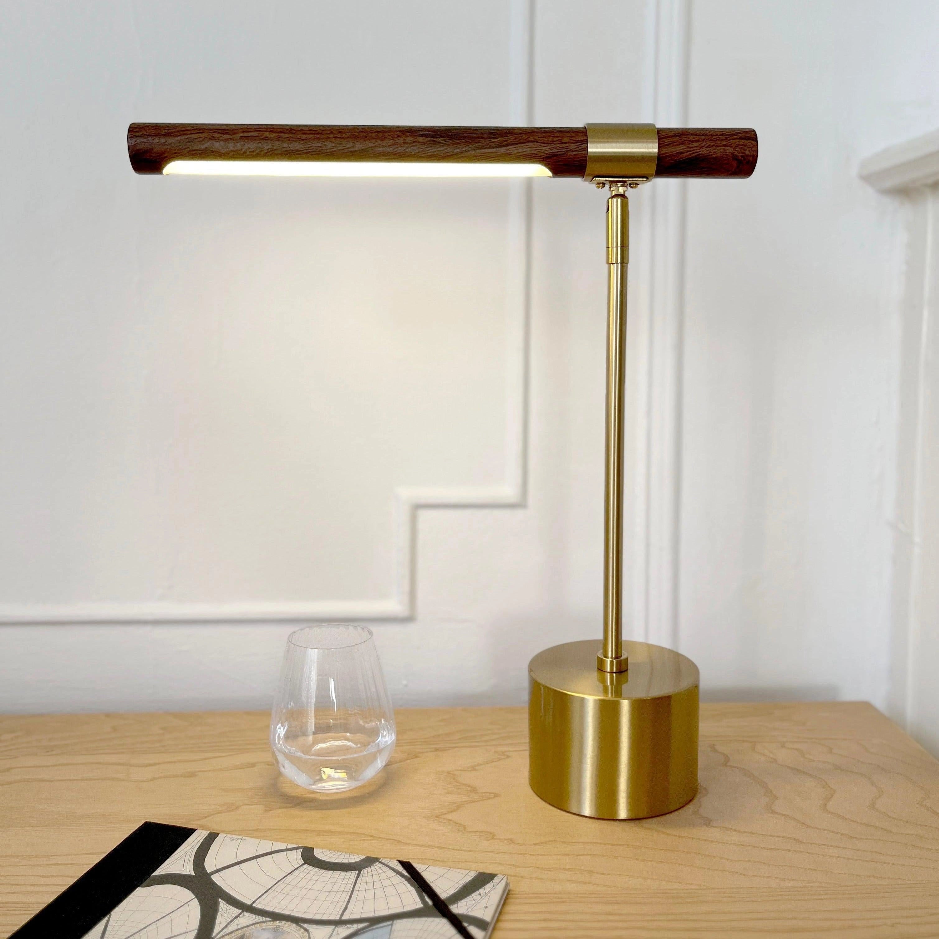 Luxury brass and wood adjustable desk lamp on a wooden table with hardwood flooring in a modern office setting.