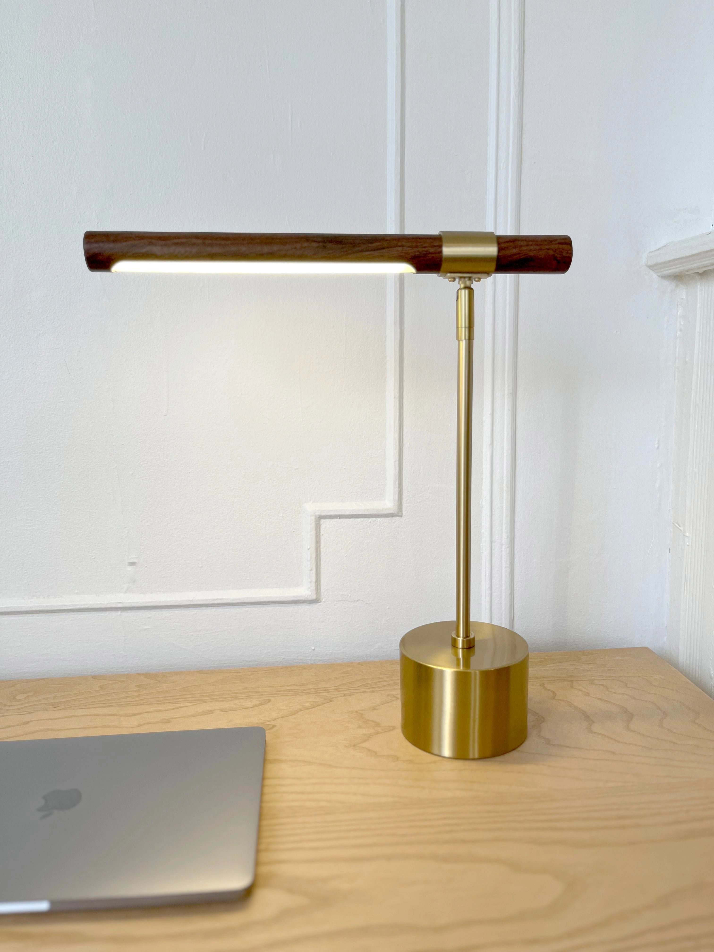 Luxury brass and wood adjustable desk lamp on a modern office table near a laptop and shelving unit.