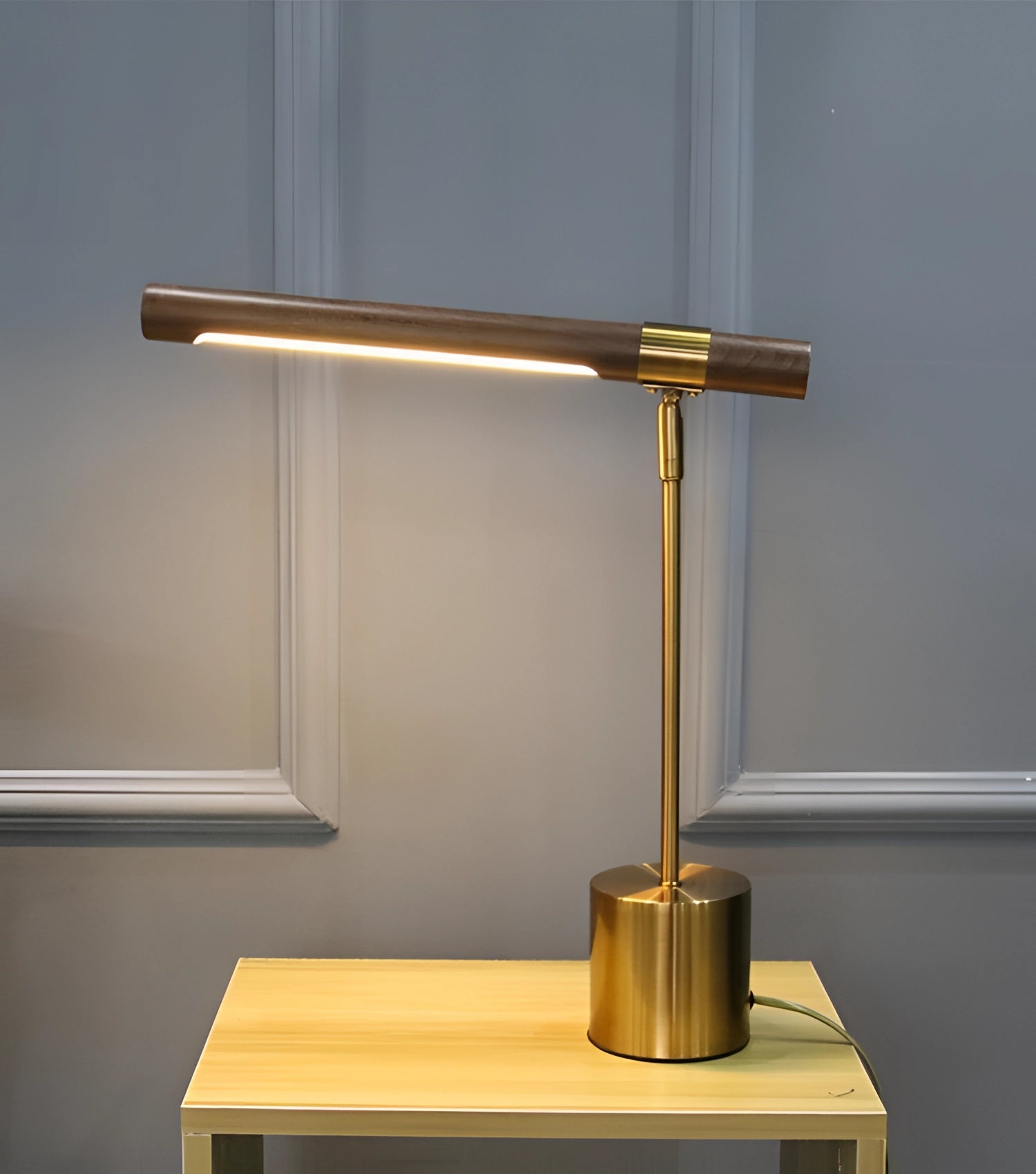 Luxury brass and wood adjustable desk lamp on a modern office table with shelving in the background.