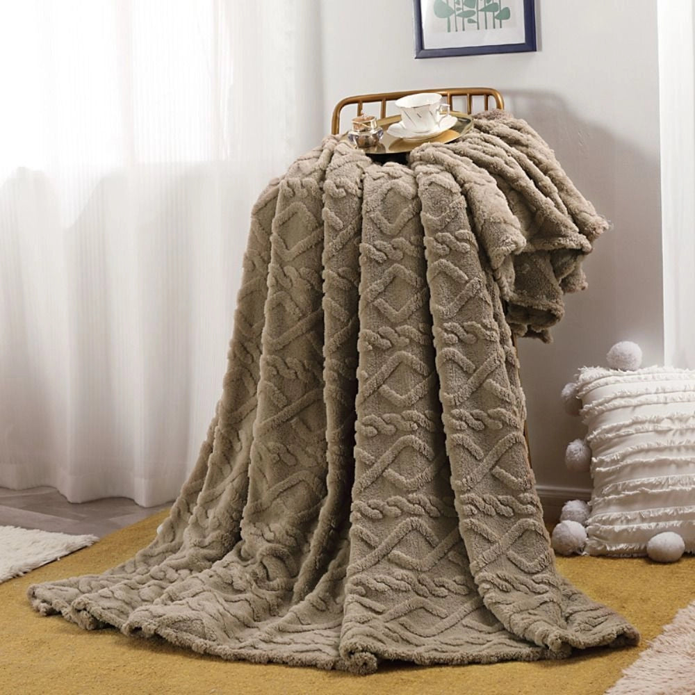 Cream luxury cable knit throw blanket draped over a dark brown wooden chair in a room with grey flooring, showcasing elegant fashion design and high-quality natural materials.