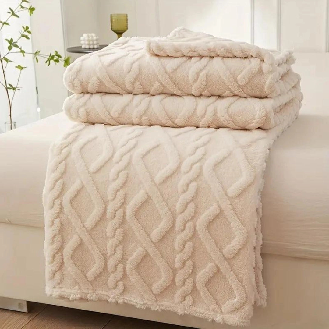 Elegant cream cable knit throw blanket draped over a wooden bed frame with beige linens and hardwood flooring.