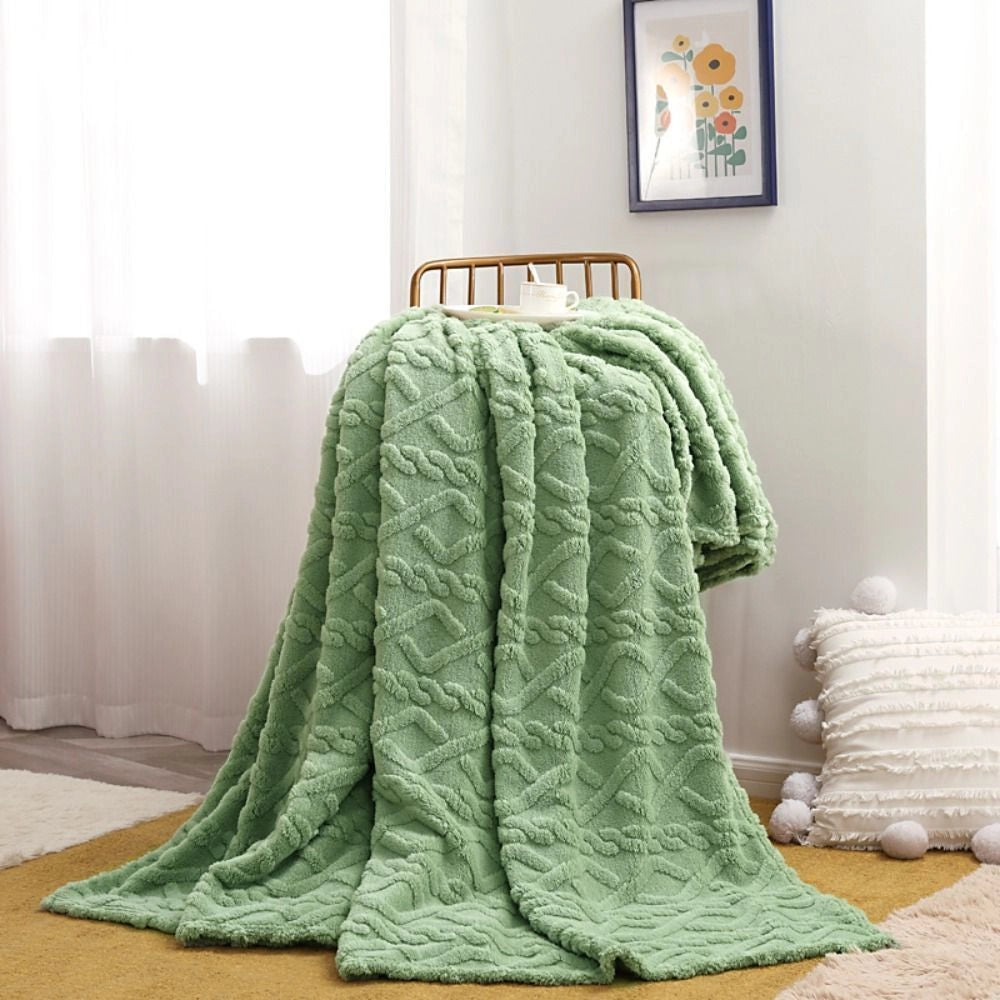 A luxurious green cable knit throw blanket, elegantly draped over a chair, showcasing its high-quality textile and cozy design. The blanket is displayed in a room with wooden flooring and decorative elements like picture frames, emphasizing comfort and natural materials. The size of the blanket is 200x230cm.