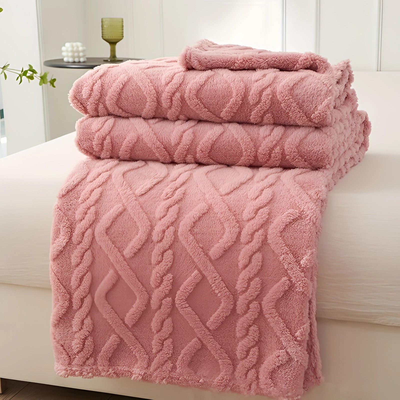 Luxury cream geometric throw blanket in pink, draped over an armchair. The plush textile adds comfort and style, with a rectangular shape complementing the furniture and floor.