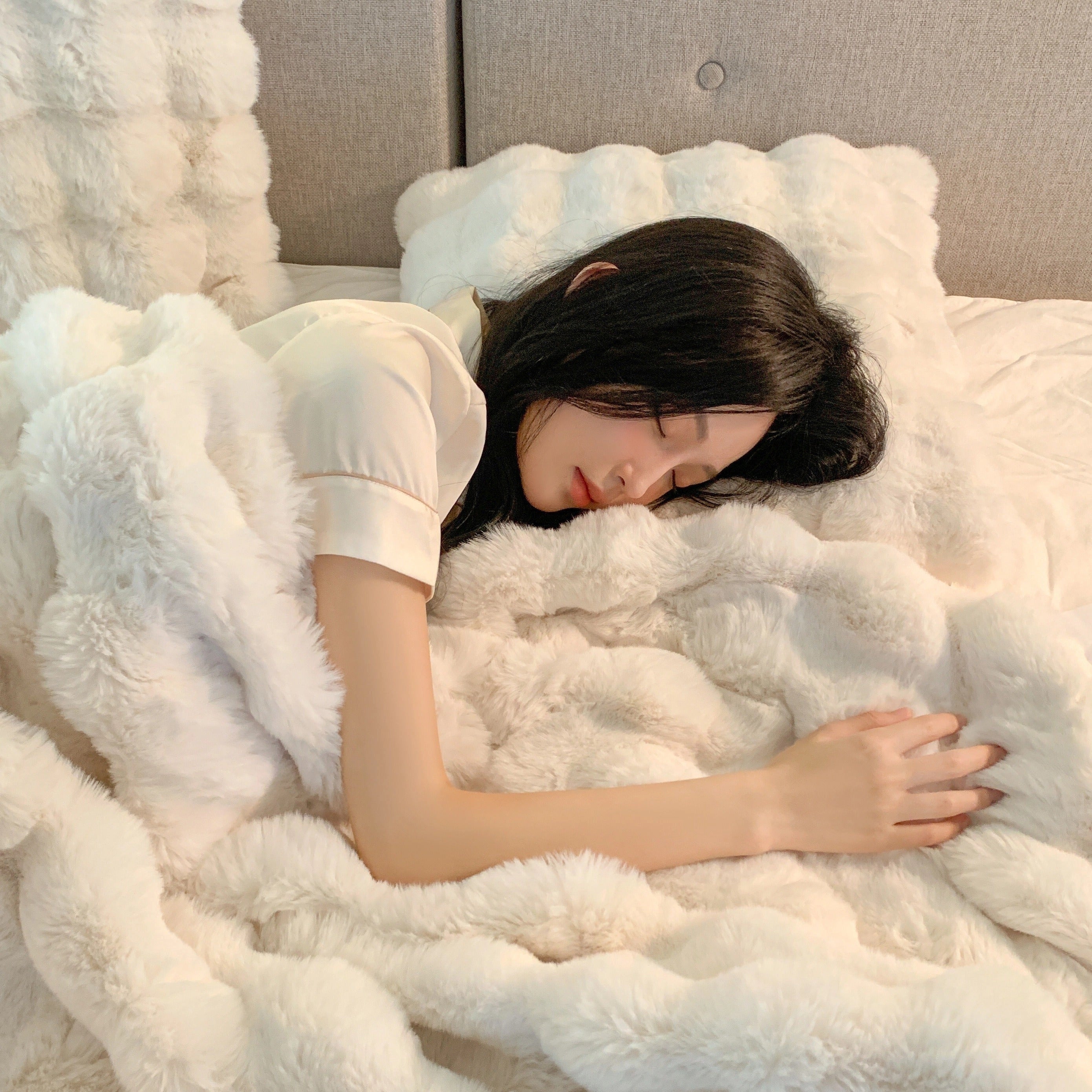 Luxurious white faux fur blanket draped over a neatly made bed, showcasing its plush and soft texture.