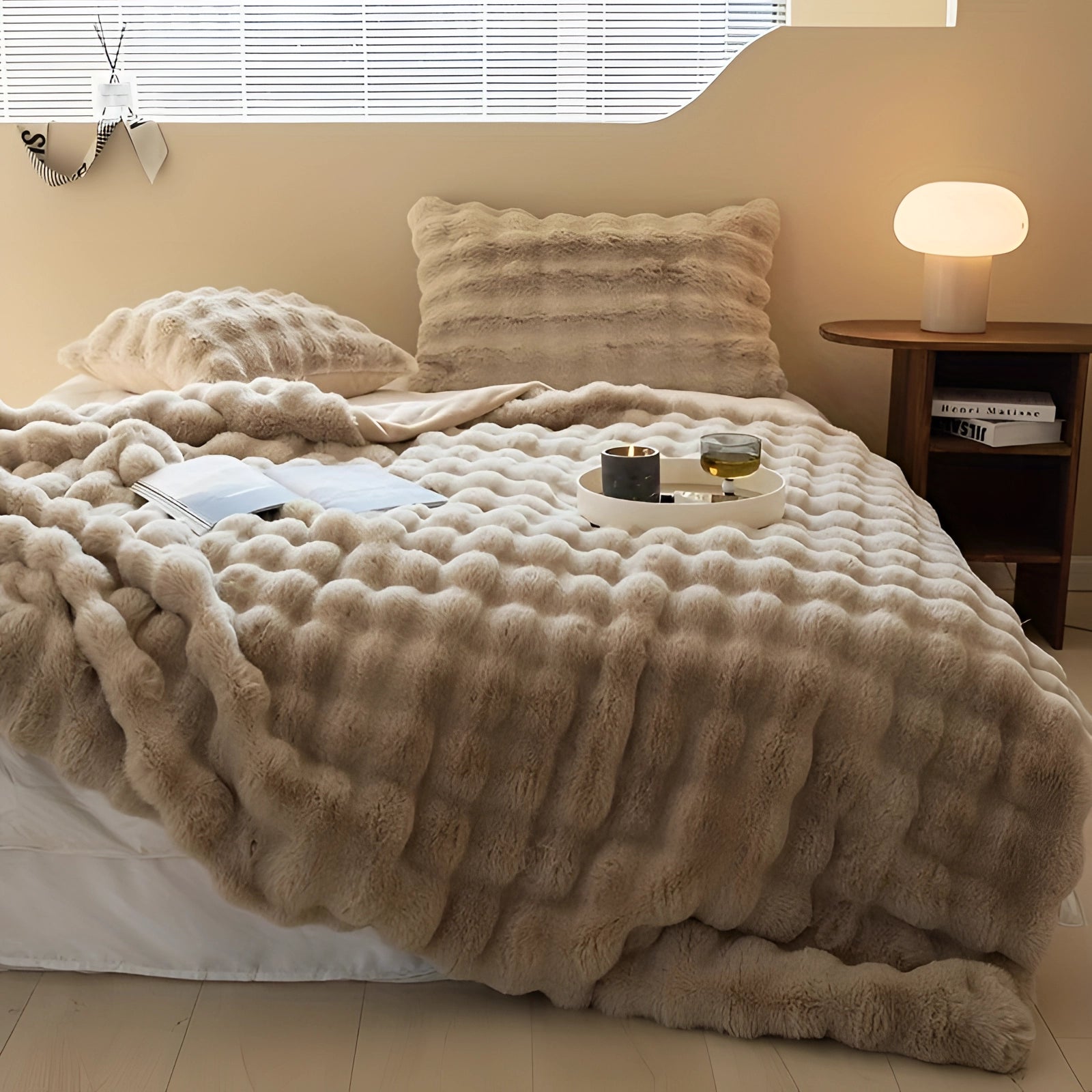 Luxurious faux fur blanket in brown and beige tones draped over a light-colored bed frame, creating a warm and comfortable bedding setup on wooden flooring.