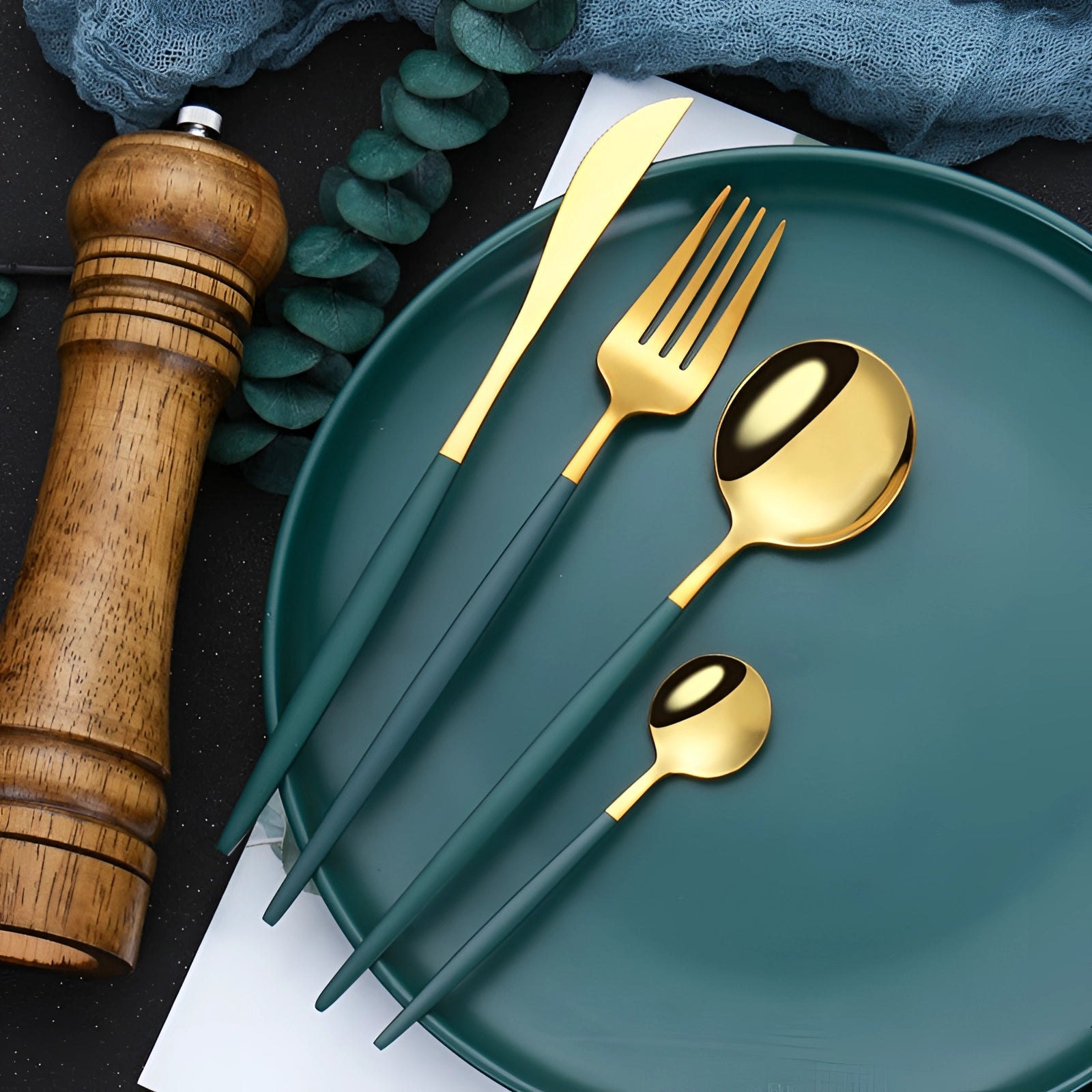 Elegant gold cutlery set with modern design, featuring a fork and table knife against a rich emerald green backdrop, complemented by stylish tableware and dishware elements.