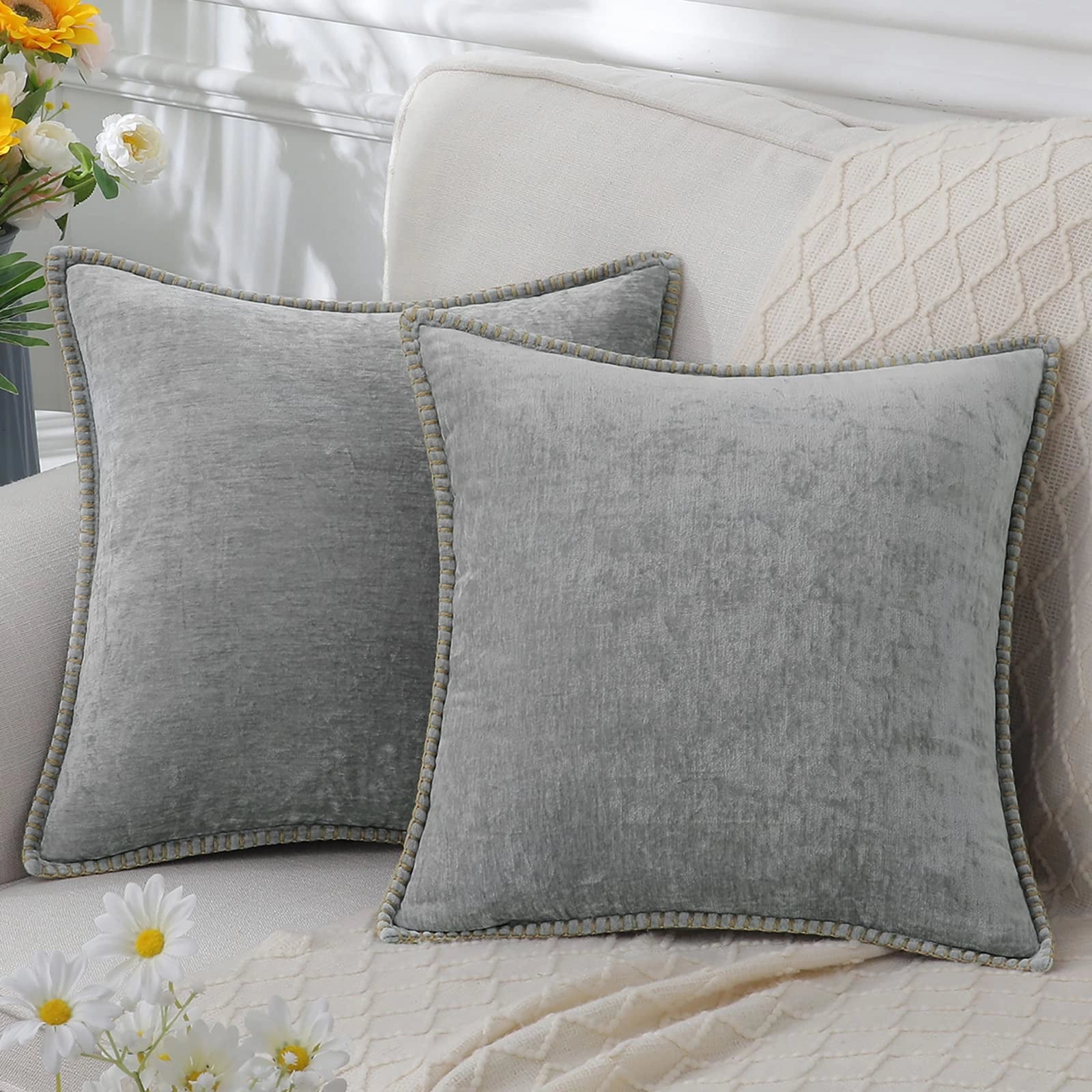 Luxury grey velvet throw pillows arranged on a white couch with a plant in the background, showcasing their elegant and soft texture.