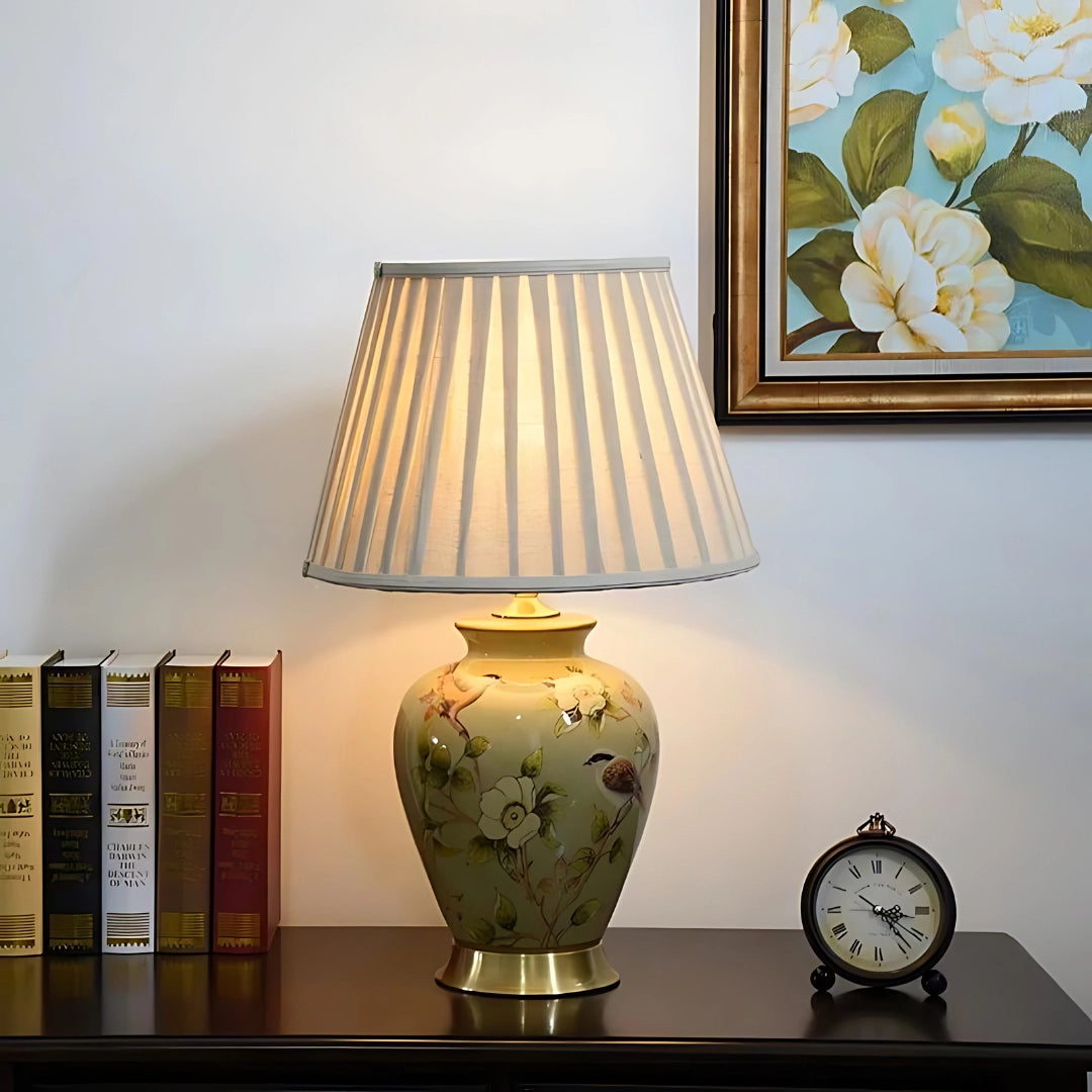 Luxury hand-painted green ceramic table lamp with gold trim, displayed on a wooden table, illuminated in an interior setting.