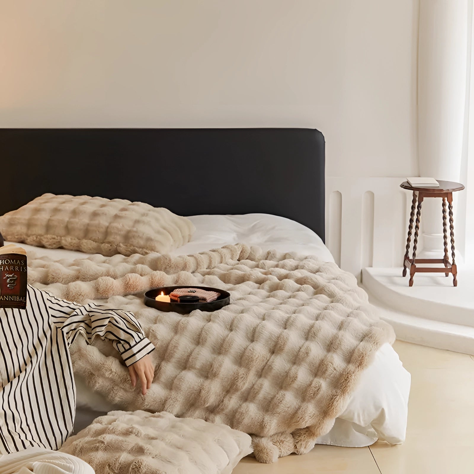 Luxury handmade chunky knit weighted blanket in a cozy designer style, draped over a brown and grey interior setting with wooden flooring and a pillow nearby.