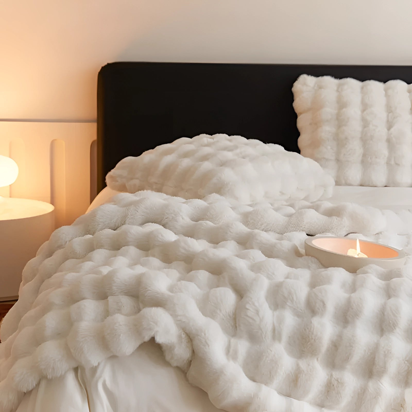 Luxurious handmade chunky knit weighted blanket draped over a neatly made bed with matching linens, surrounded by wooden furniture, including a bed frame and a lamp, creating a cozy and inviting bedroom atmosphere.