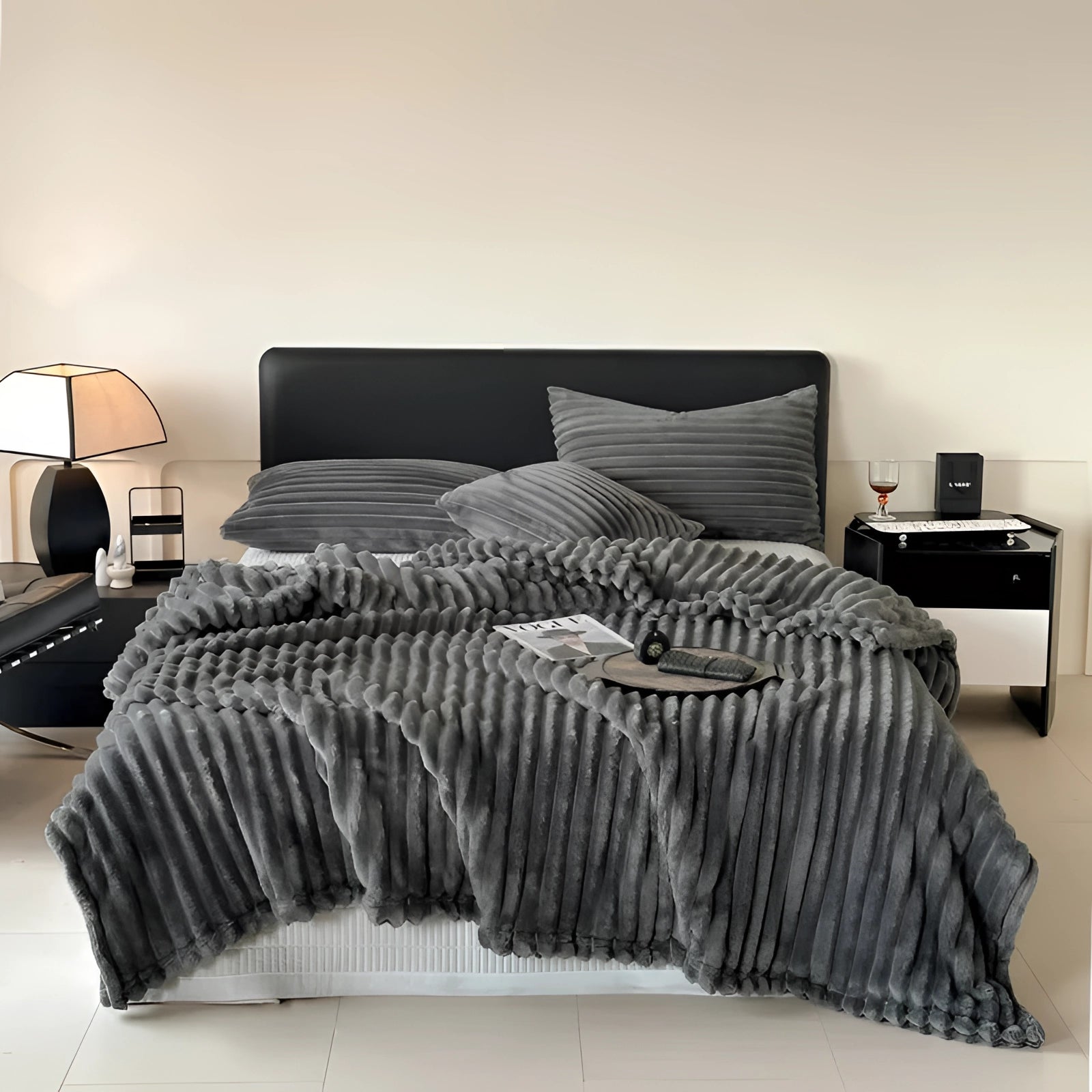 Luxury handmade chunky knit wool blanket in grey draped over a wooden bed frame in a cozy interior setting. The oversized throw, measuring 230cm by 250cm, adds warmth and comfort to the room's design, complemented by neutral flooring.