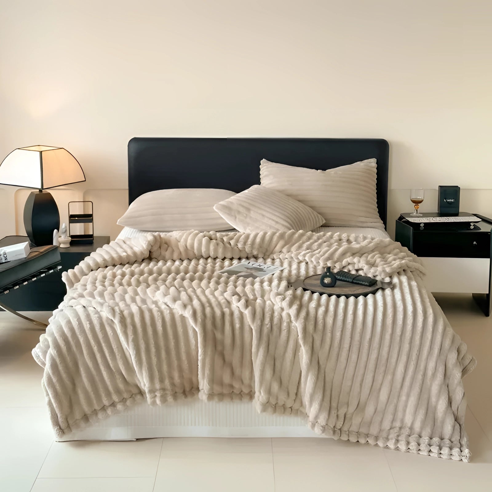 Luxury handmade chunky knit wool blanket in grey, draped over a wooden bed frame in a cozy bedroom setting with a lamp on a wooden floor. The oversized throw measures 230cm x 250cm, adding warmth and texture to the room.