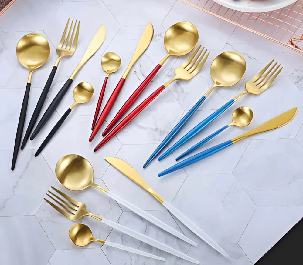 
A set of luxury metallic finish cutlery, including forks and other utensils, displayed elegantly on a wooden table alongside a yellow plate and other tableware, showcasing a stylish and durable dining experience.