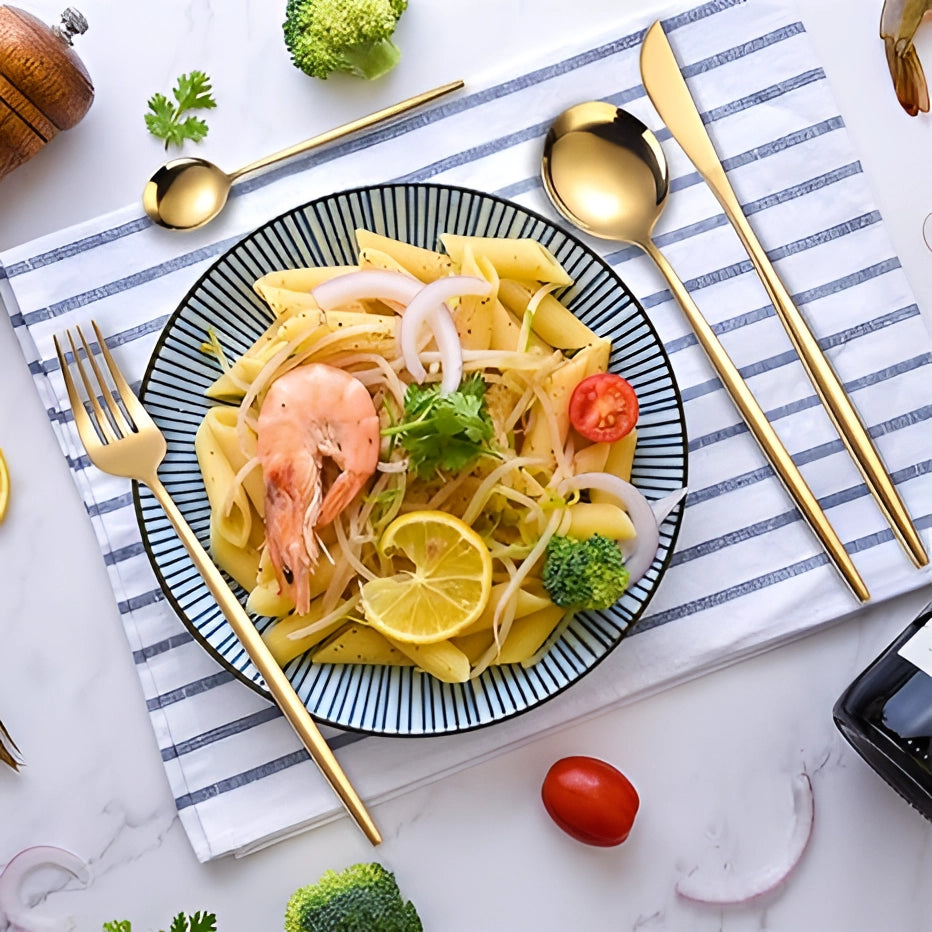 Luxury metallic finish cutlery set displayed on a dining table alongside a plate with food, featuring a fork and other tableware items.