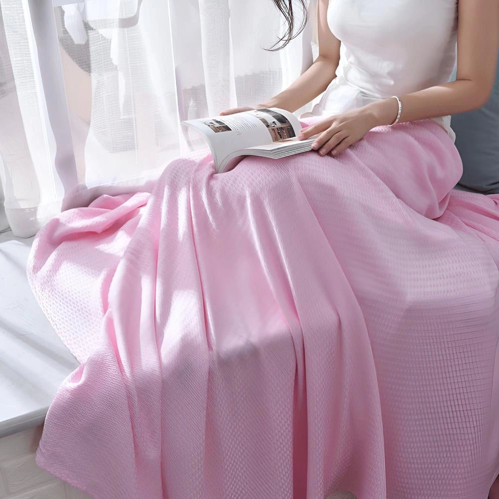 Luxurious pink textured blanket draped over a bed, showcasing its elegant summer throw design. The blanket is neatly folded, emphasizing its soft texture and quality material suitable for a queen-sized bed.