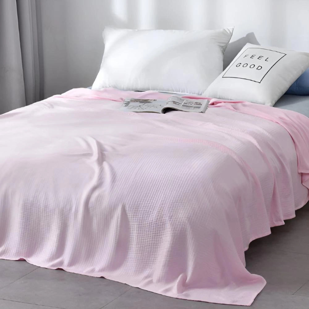 A rose pink luxury textured blanket elegantly draped over a queen-sized bed, complemented by soft pillows, creating a serene and inviting bedroom atmosphere.