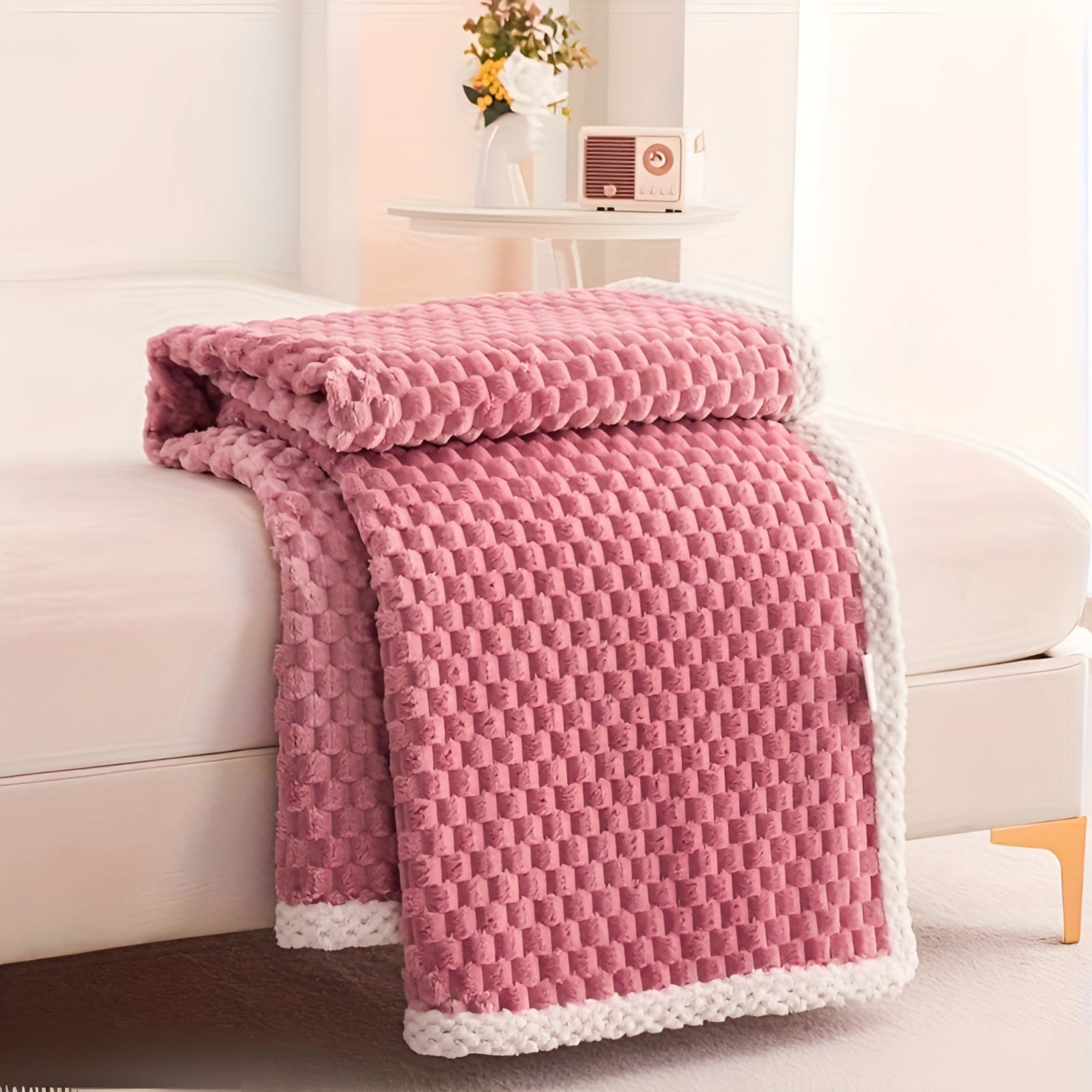 Luxurious pink textured blanket with pom-pom trim draped over a wooden floor, featuring a cozy and plush knitted design, set in a stylishly designed interior space.