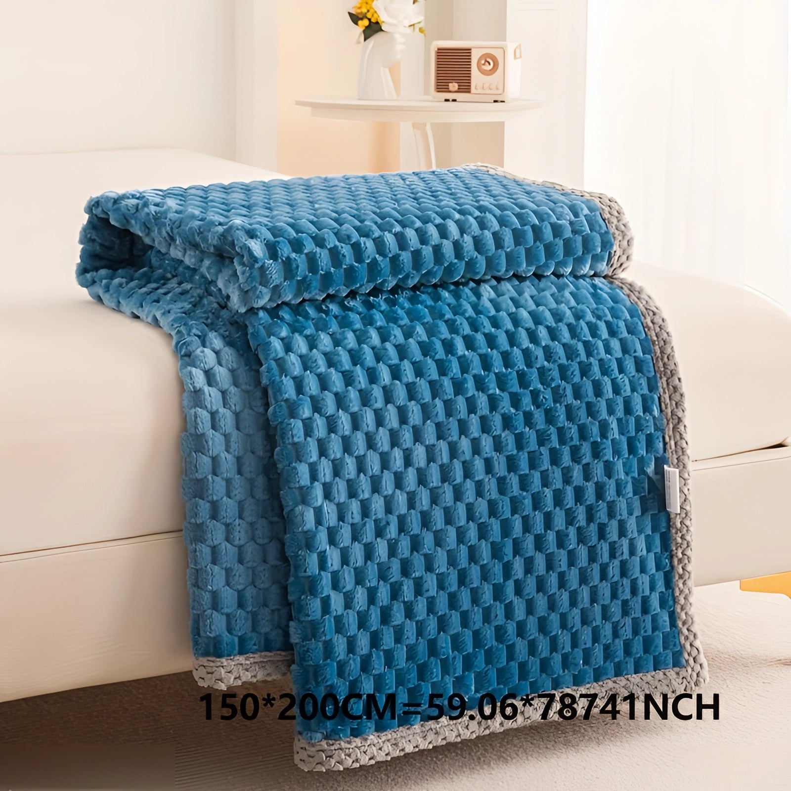 Luxury blue textured blanket with a plush, cozy knitted design and pom-pom trim, displayed on a wooden floor.