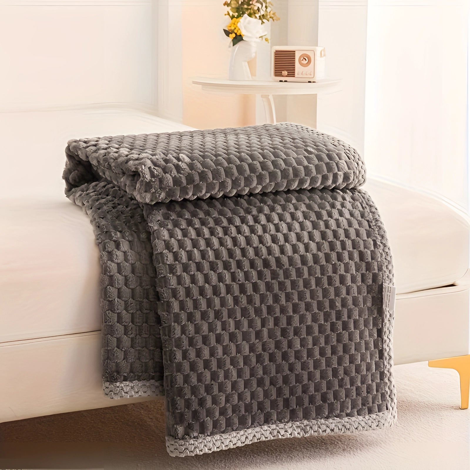 Luxury gray textured blanket draped elegantly over hardwood flooring, showcasing plush cozy knitted fabric with a charming pom-pom trim.