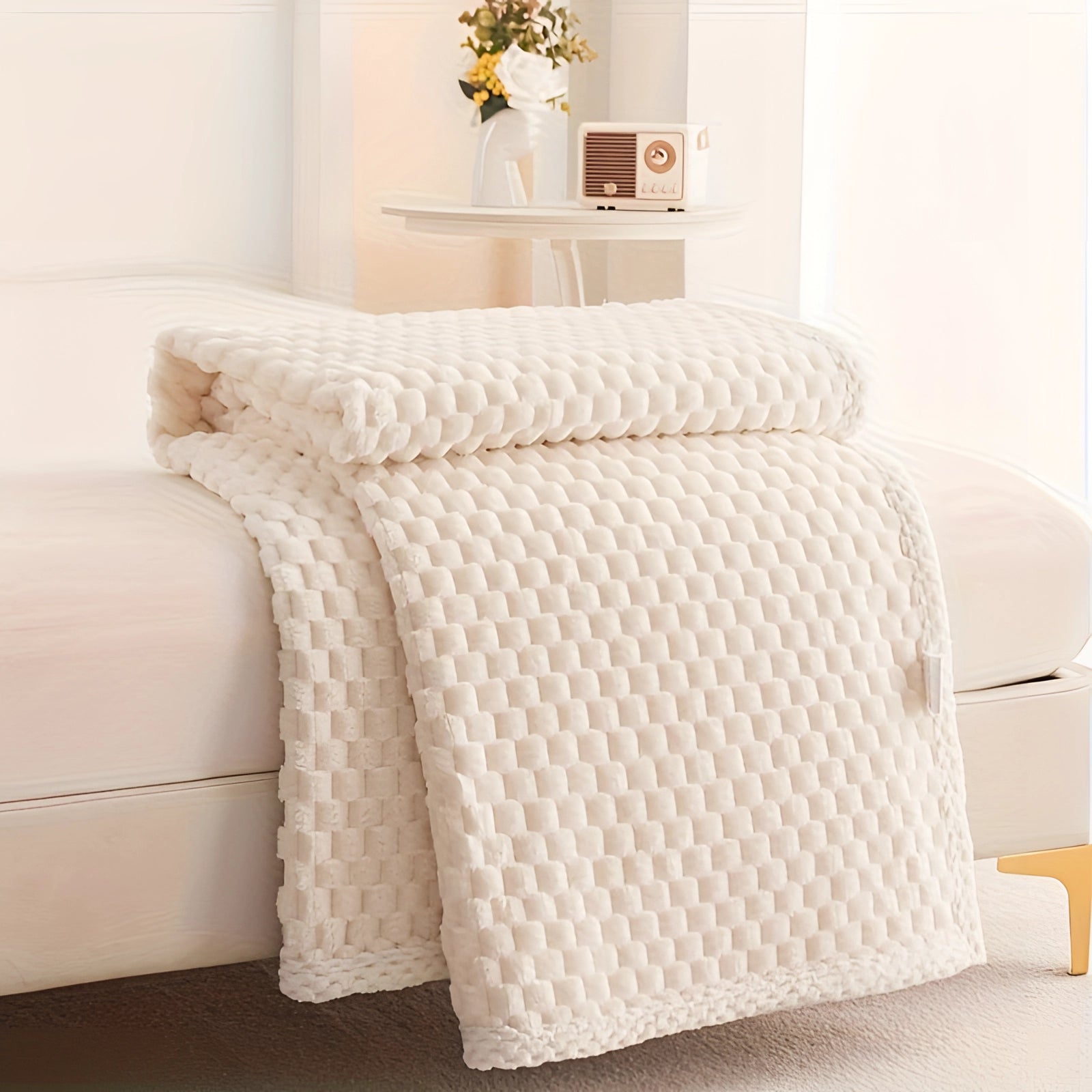 Luxurious milk white textured blanket measuring 200 x 230 cm, elegantly draped over a bed frame in a cozy interior setting, featuring a plush, knitted design with a charming pom-pom trim next to a wooden floor and plant decor.