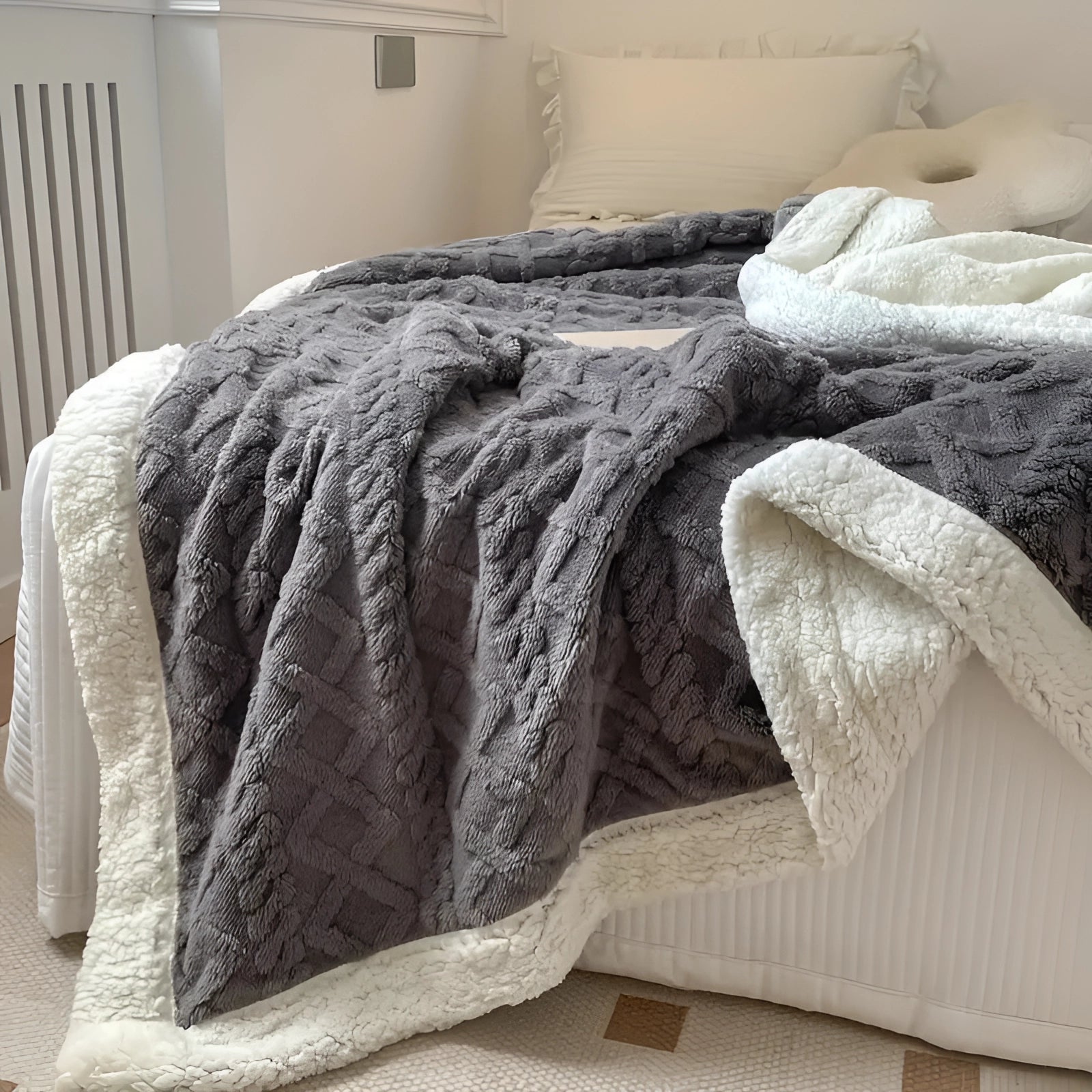 Luxurious gray reversible sherpa fleece blanket draped over the back of a wooden furniture piece, showcasing its cozy and soft texture, with a hardwood floor in the background.