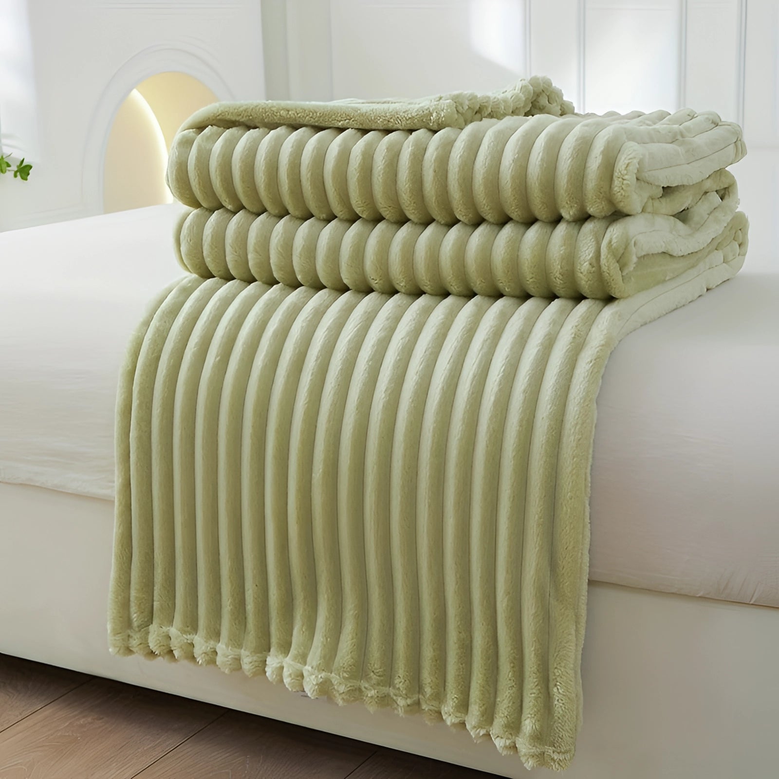 Luxurious green velvet ribbed throw blanket draped over a studio couch placed on hardwood flooring, providing a cozy and decorative accent to the room.