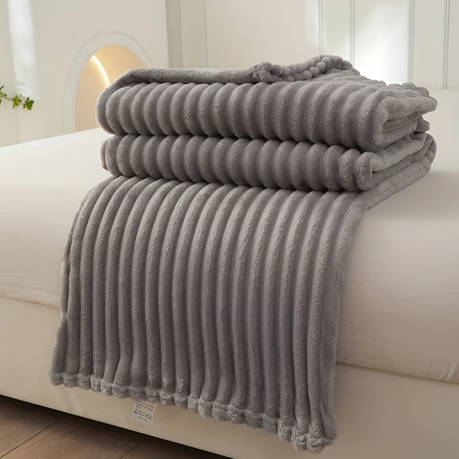 Royal blue velvet ribbed throw blanket draped over a light gray couch, featuring a soft and cozy texture. The setting includes a studio couch with elegant wooden elements and a nearby grey ottoman, creating a comfortable and stylish living area.