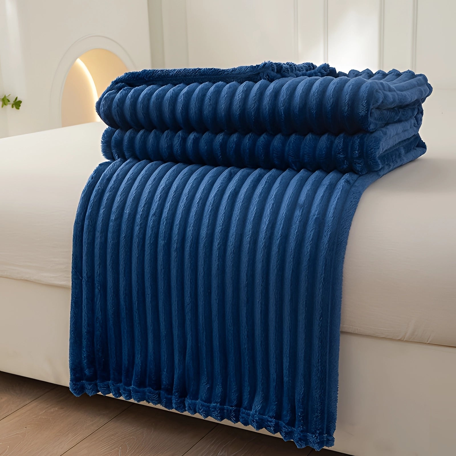 Luxurious royal blue velvet ribbed throw blanket draped elegantly over a grey couch, highlighting its rich azure color and soft texture, adding a cozy decorative accent to the furniture in a stylish living room setting.