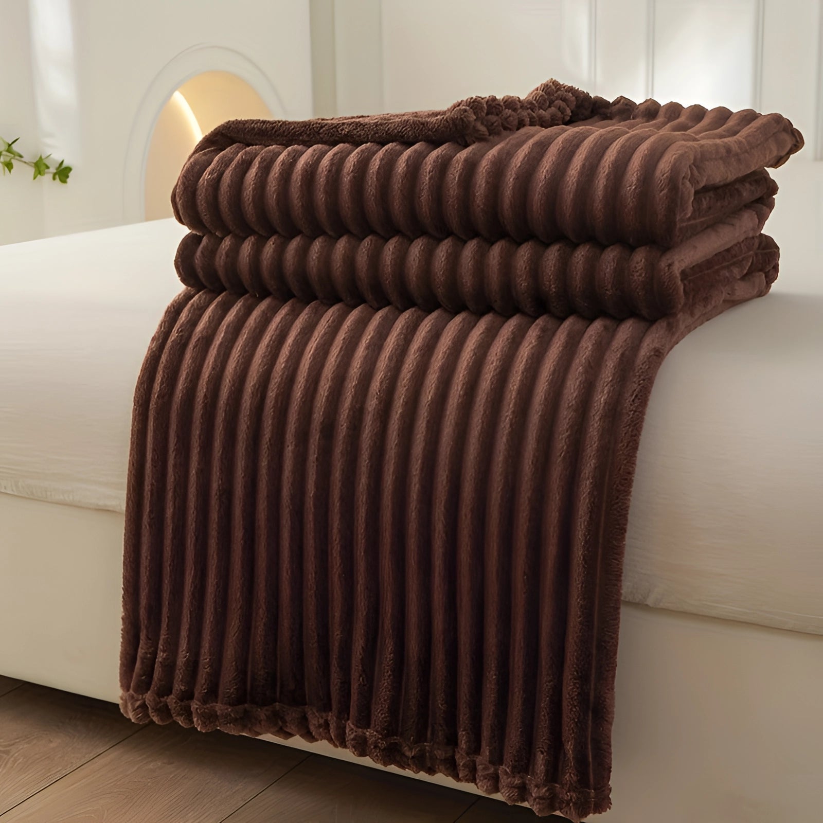 Luxury royal blue velvet ribbed throw blanket elegantly draped over a brown couch with wooden armrests, adding a cozy decorative accent to the living room setting.