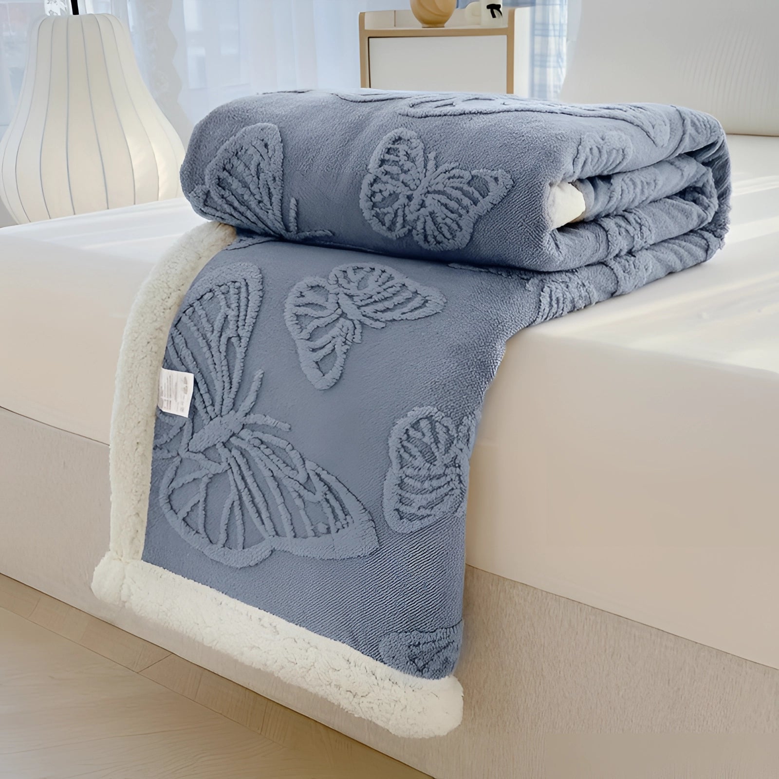 
A plush gray leaves throw luxury sherpa fleece blanket draped over a couch with a misty orchid hue, sized 200*230cm. The blanket is surrounded by furniture including a wooden table and a pillow, adding comfort and style to the setting.