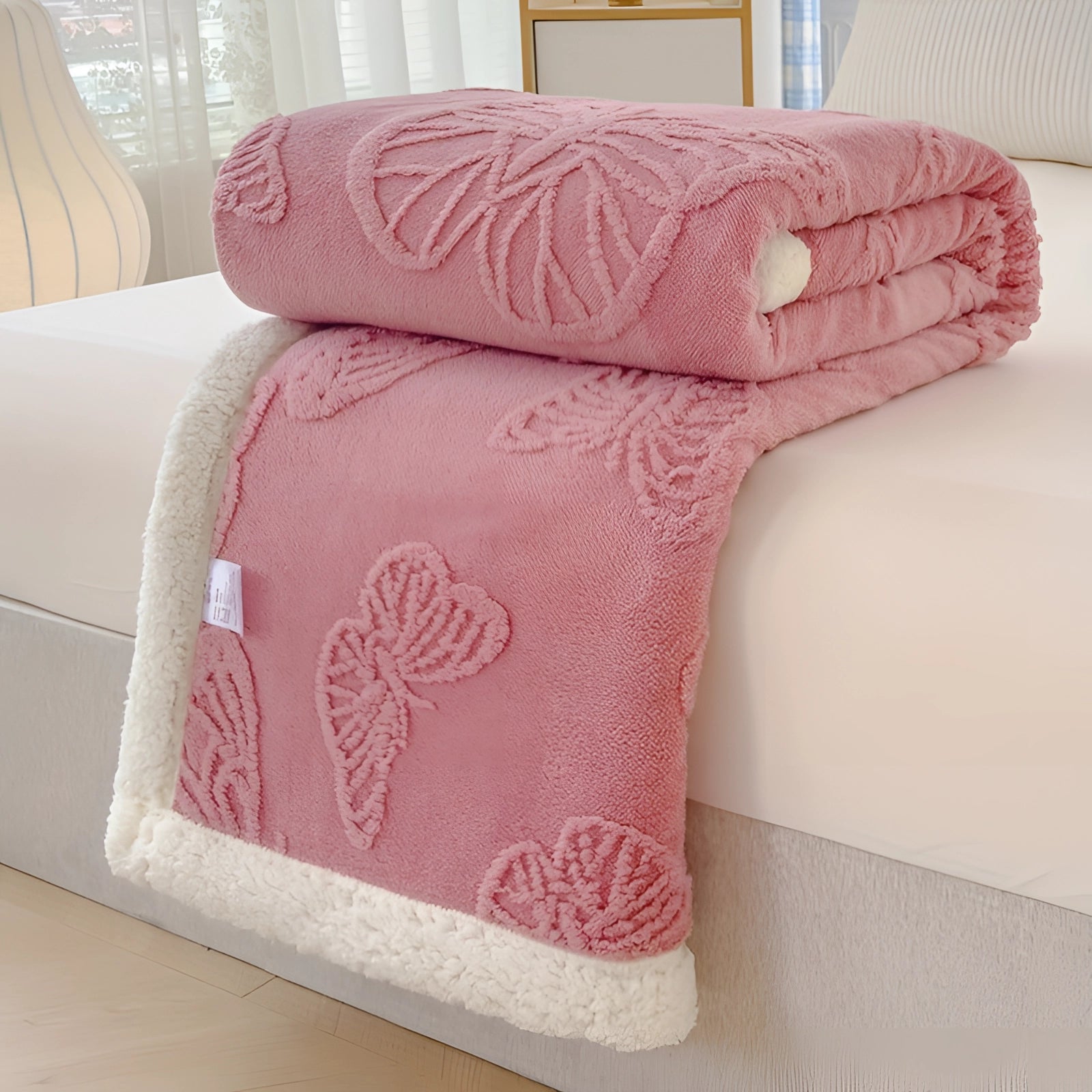 A pink luxury sherpa fleece blanket with plush gray leaf patterns draped over a couch in a cozy living room setting.