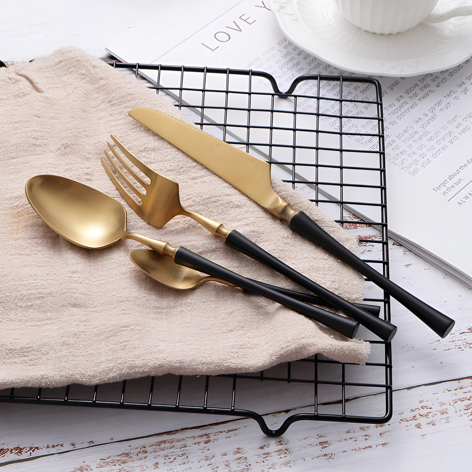 Elegant matte gold and black stainless steel cutlery set displayed on a beige tablecloth, showcasing luxury tableware designed for fine dining experiences.