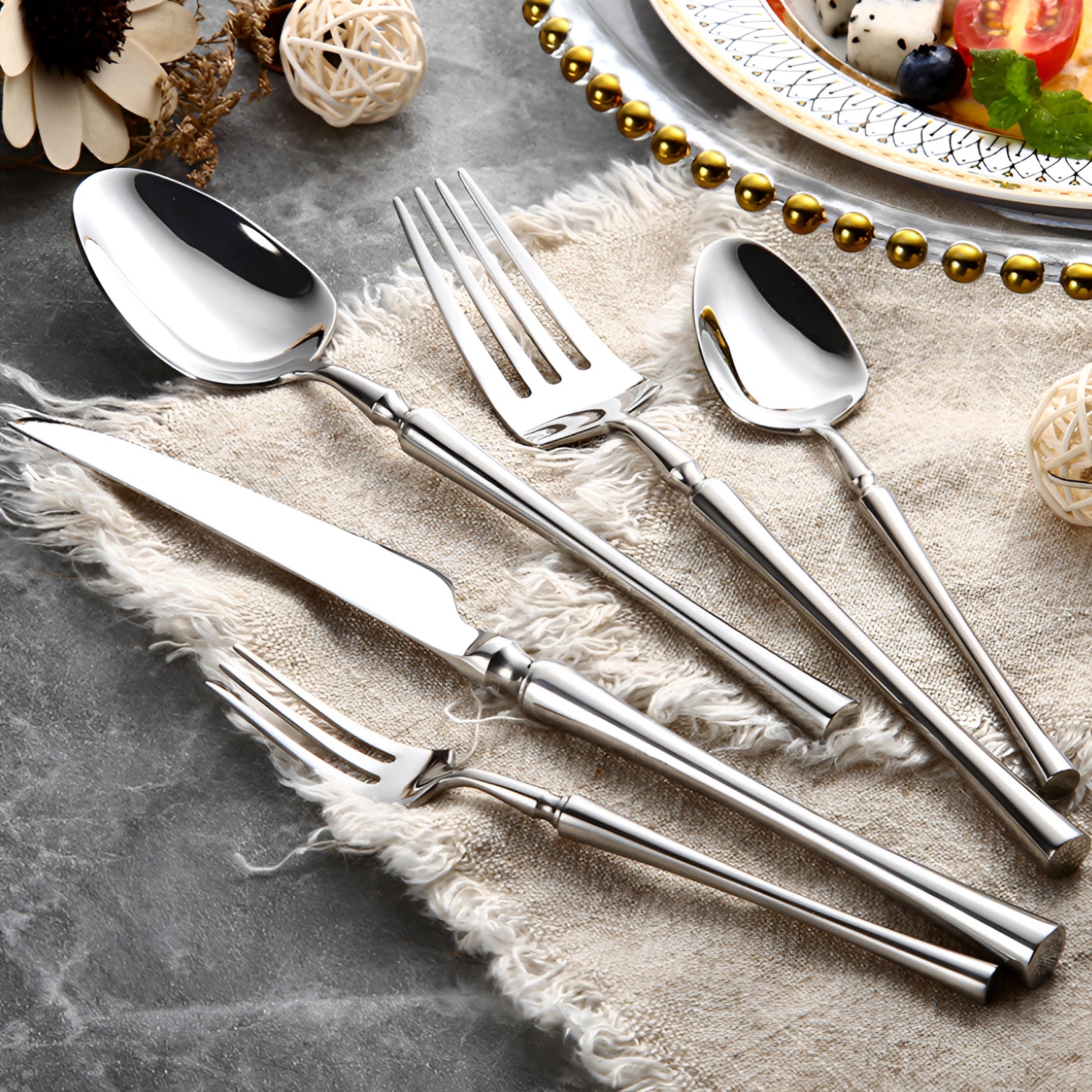 Luxury silver cutlery set featuring elegant stainless steel silverware, including forks and table knives, arranged on a table with a white tablecloth, accompanied by dishware and a plate.