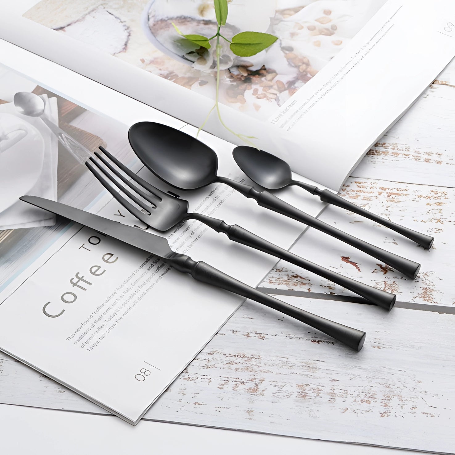 Luxury matte black cutlery set with a sleek, elegant design, featuring forks, knives, and spoons made from high-quality stainless steel, arranged artfully alongside a rectangular plate on a dining table.