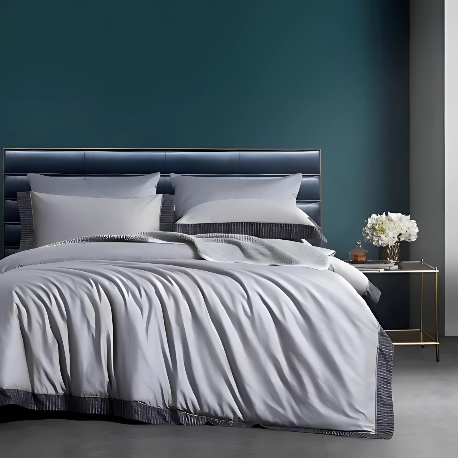 Luxury king-size bedding set featuring an elegant teal blue comforter with matching pillowcases, set against a gray bed frame. The scene includes a wooden bed frame and a cozy ambiance with a lamp and decorative elements like picture frames.