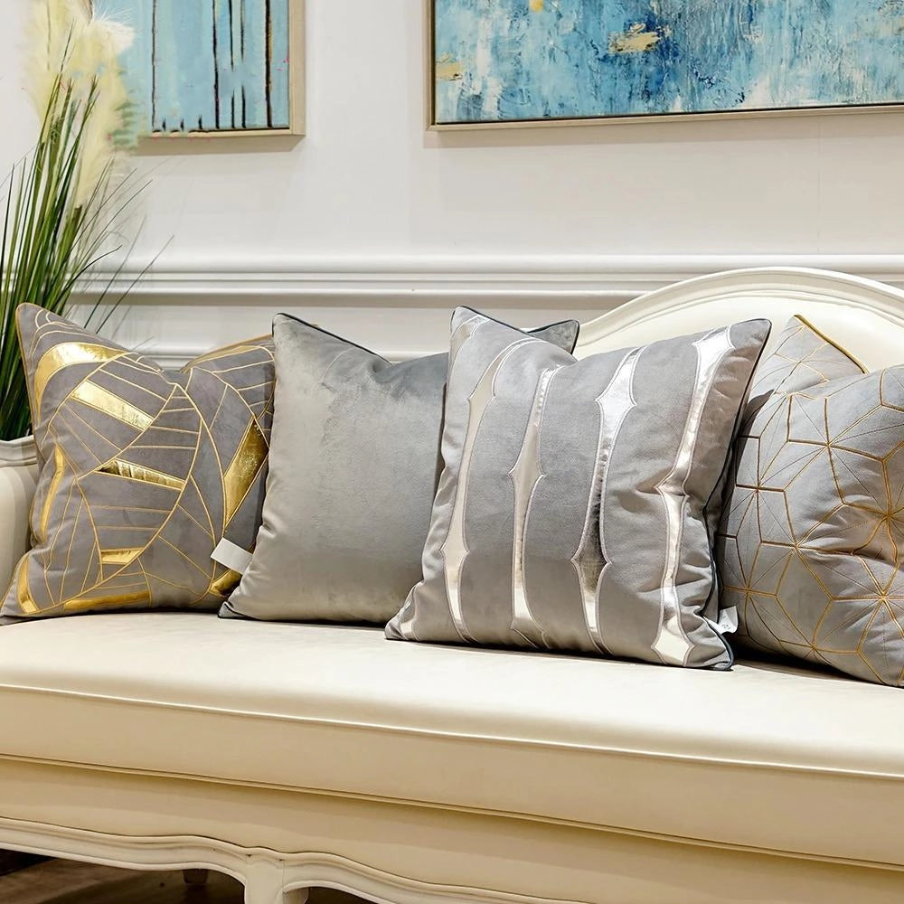 Luxury velvet throw pillows with gold accent geometric patterns placed on a stylish couch, surrounded by a cozy setting that includes a plant, a window with natural light, and wooden elements, creating a comfortable and elegant living space.